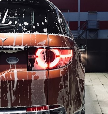 Rear of a dark red car being rinsed with soapy water.
