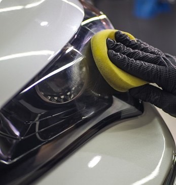 Hand polishing a car headlight with a yellow applicator pad.